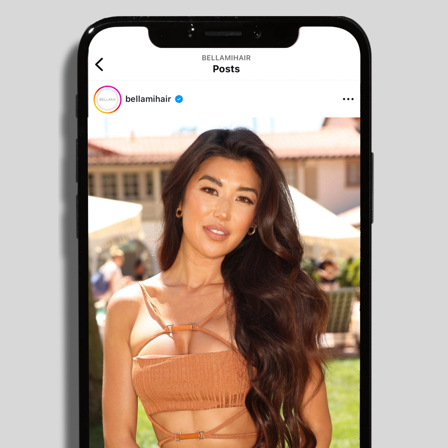 Instagram post on a smartphone showing a woman with long, wavy dark hair by the verified account bellamihair.