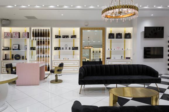 Bellami salon with black velvet sofas, gold tables, chandelier, white shelves, mirror, and pink seating.